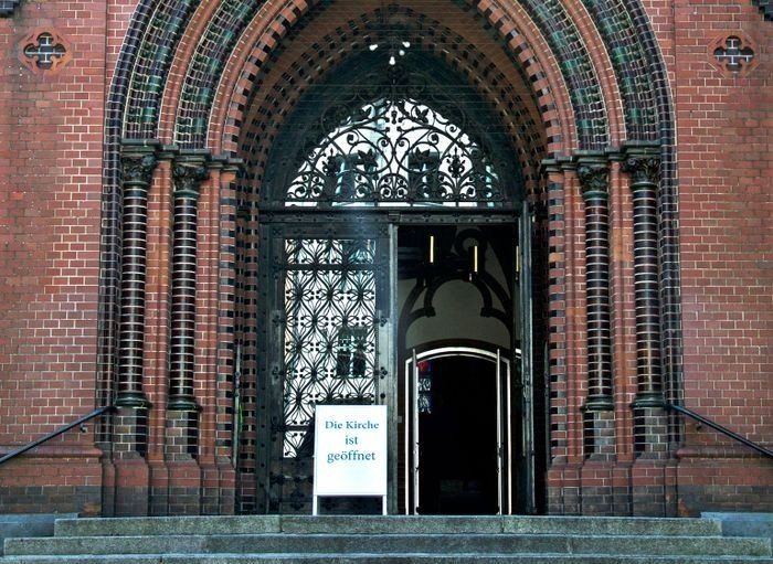 Foto vom Eingangsportal der Apostel-Paulus-Kirche mit Aufsteller "Die Kirche ist geöffnet"